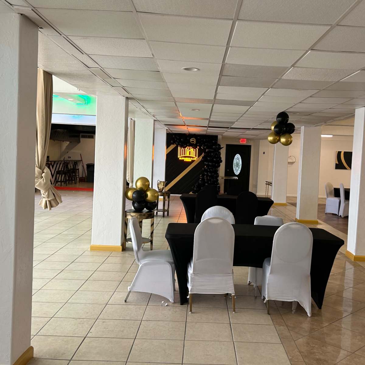 A large, open event space with tables dressed in black and white, and balloons arranged on the ceiling.