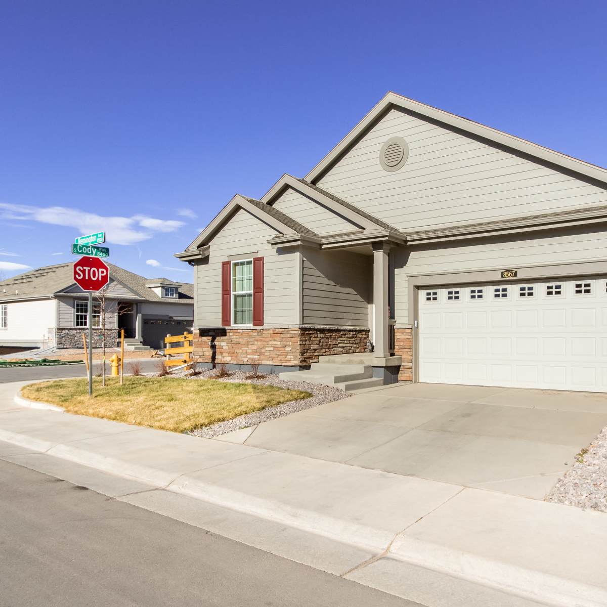 A single-story house with a light green exterior and a garage is situated at the corner of a street with a stop sign.