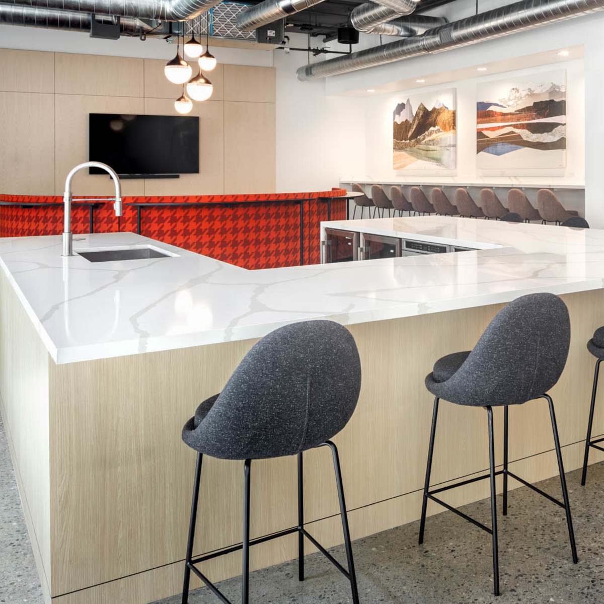 A modern kitchen area features a large white countertop with black barstools and a kitchenette in the background adorned with artwork.