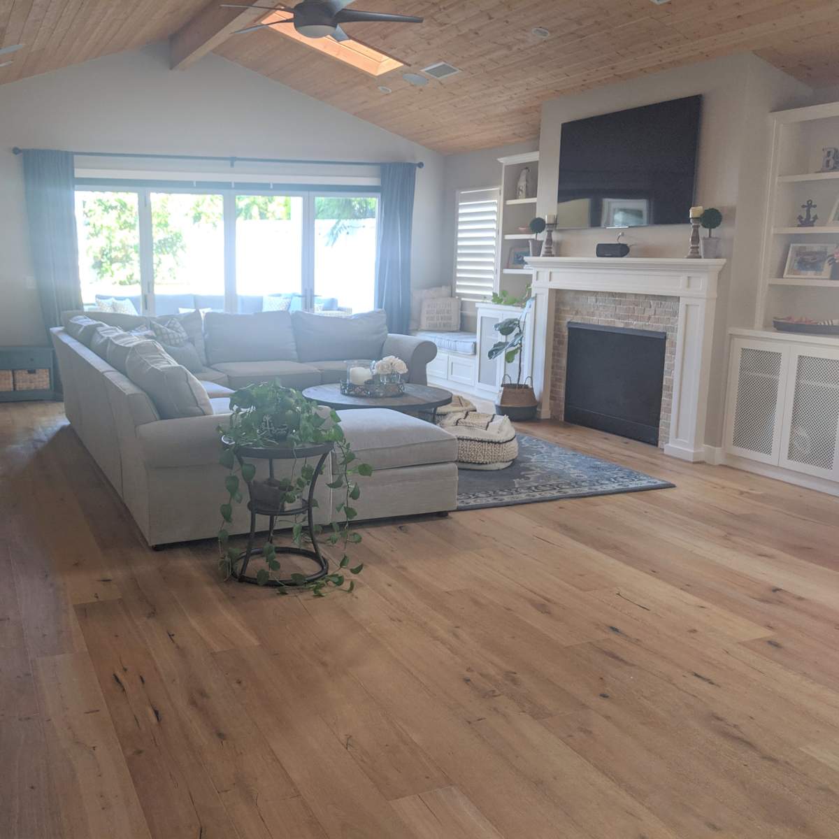 A light-filled living room with a large sectional sofa, a round coffee table, a fireplace, and large windows overlooking a view.