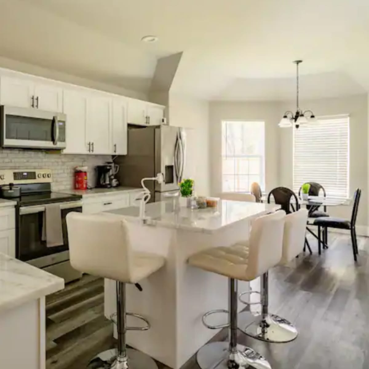 A modern kitchen with white cabinets, stainless steel appliances, a marble countertop, and a dining area with a round table and black chairs.
