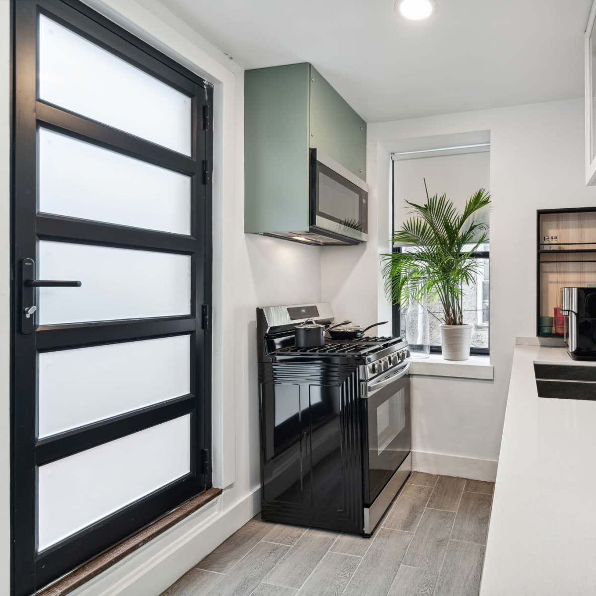 A modern kitchen featuring a black stove and sink, green cabinetry, and a large window with a potted plant on the sill.