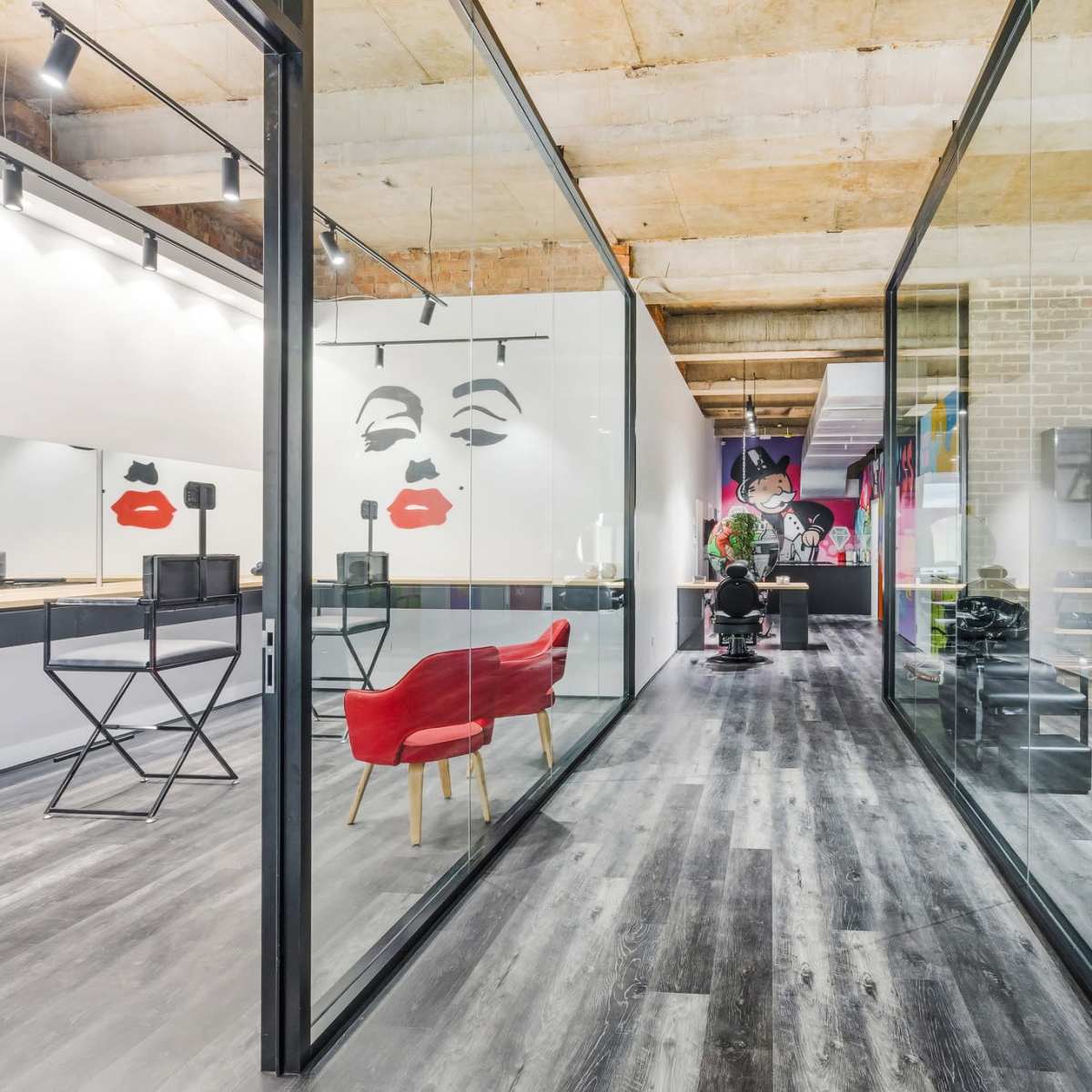 A modern salon interior with glass partitions, featuring colorful wall art and an area with styling stations and furniture.