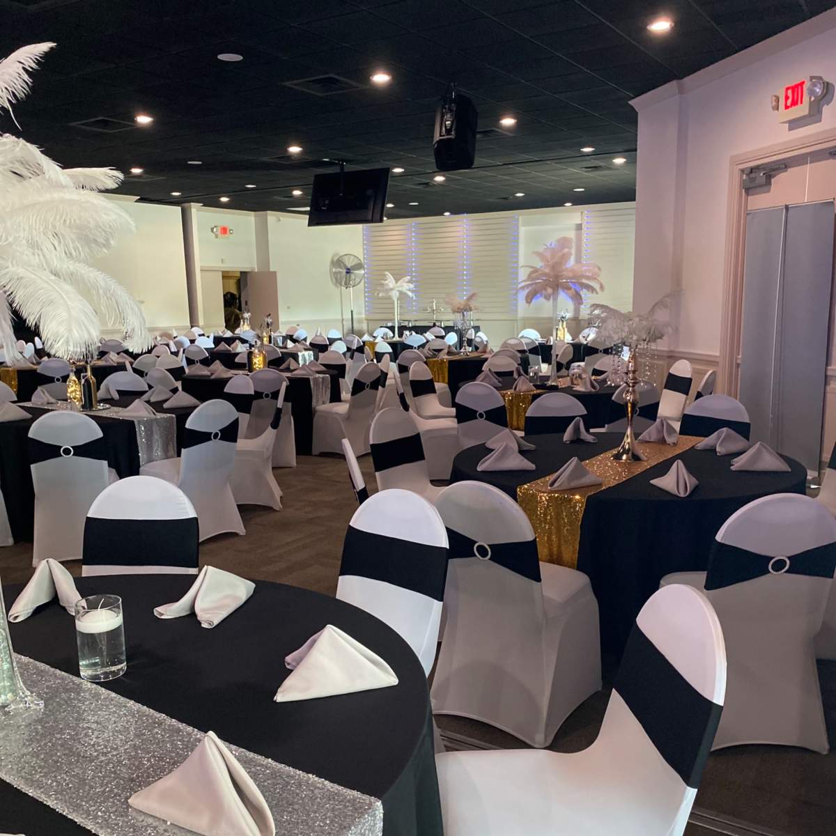 A banquet hall arranged with tables covered in black and white tablecloths and decorated with napkins and centerpieces.