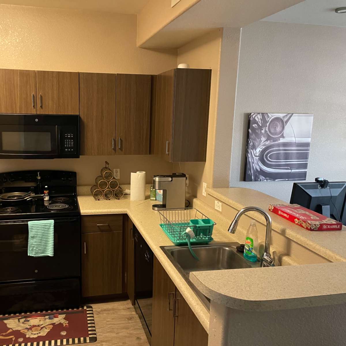 A compact kitchen with dark wood cabinetry, a black stove and microwave, and a countertop with a sink and various kitchen items.