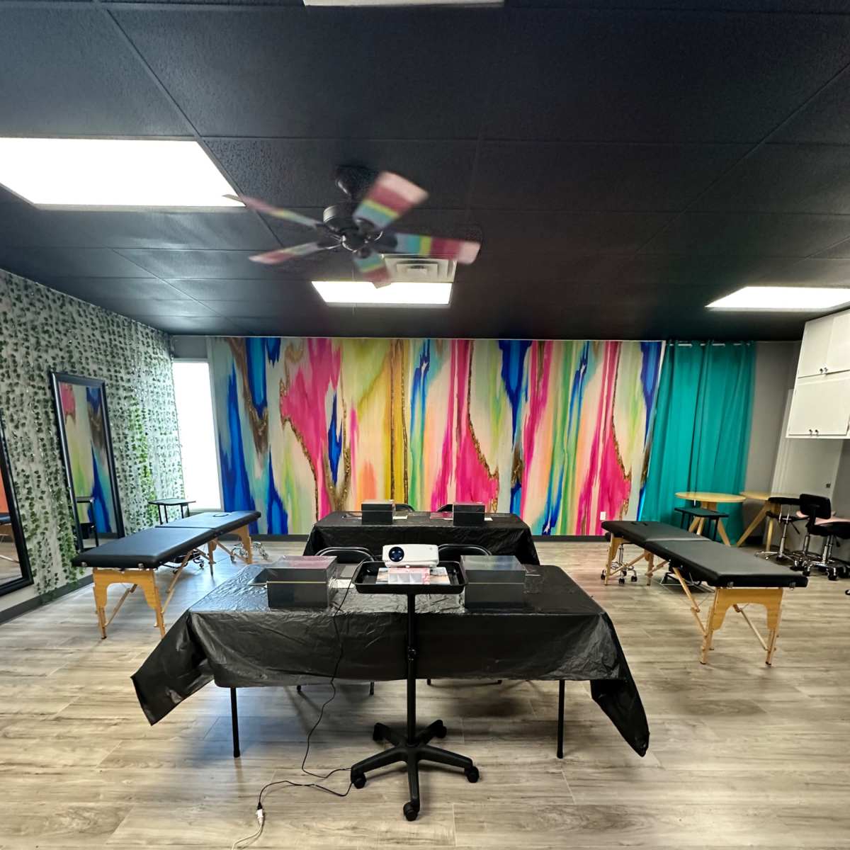 A spacious treatment room with several massage tables arranged under a colorful, abstract wall mural.