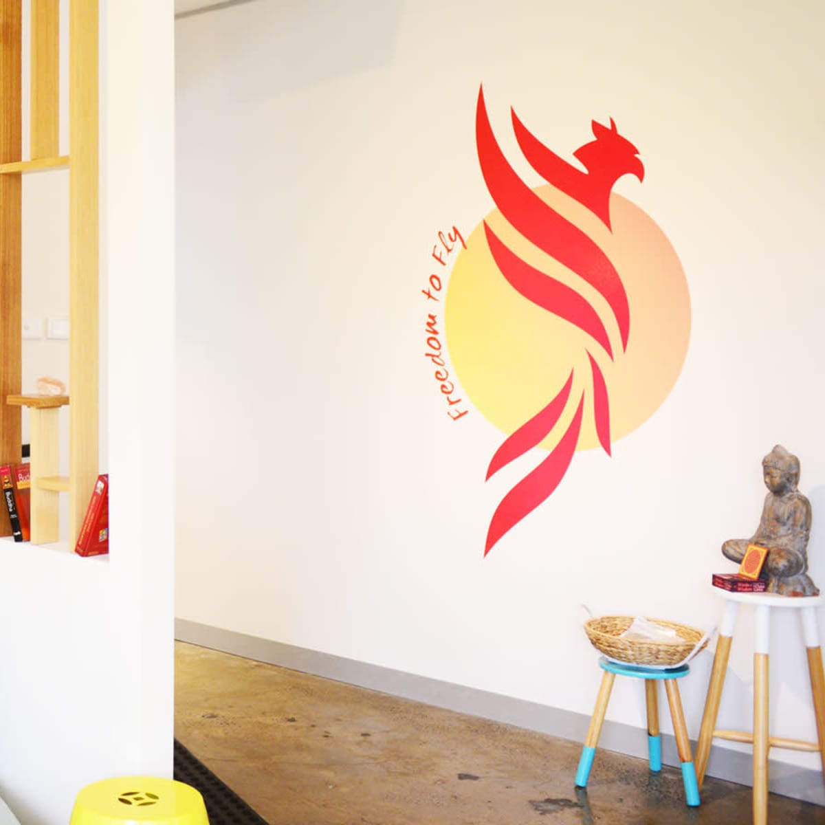 A cozy interior space featuring a light blue couch, decorative wall designs, and a vibrant mural of a phoenix with the phrase "freedom to fly."