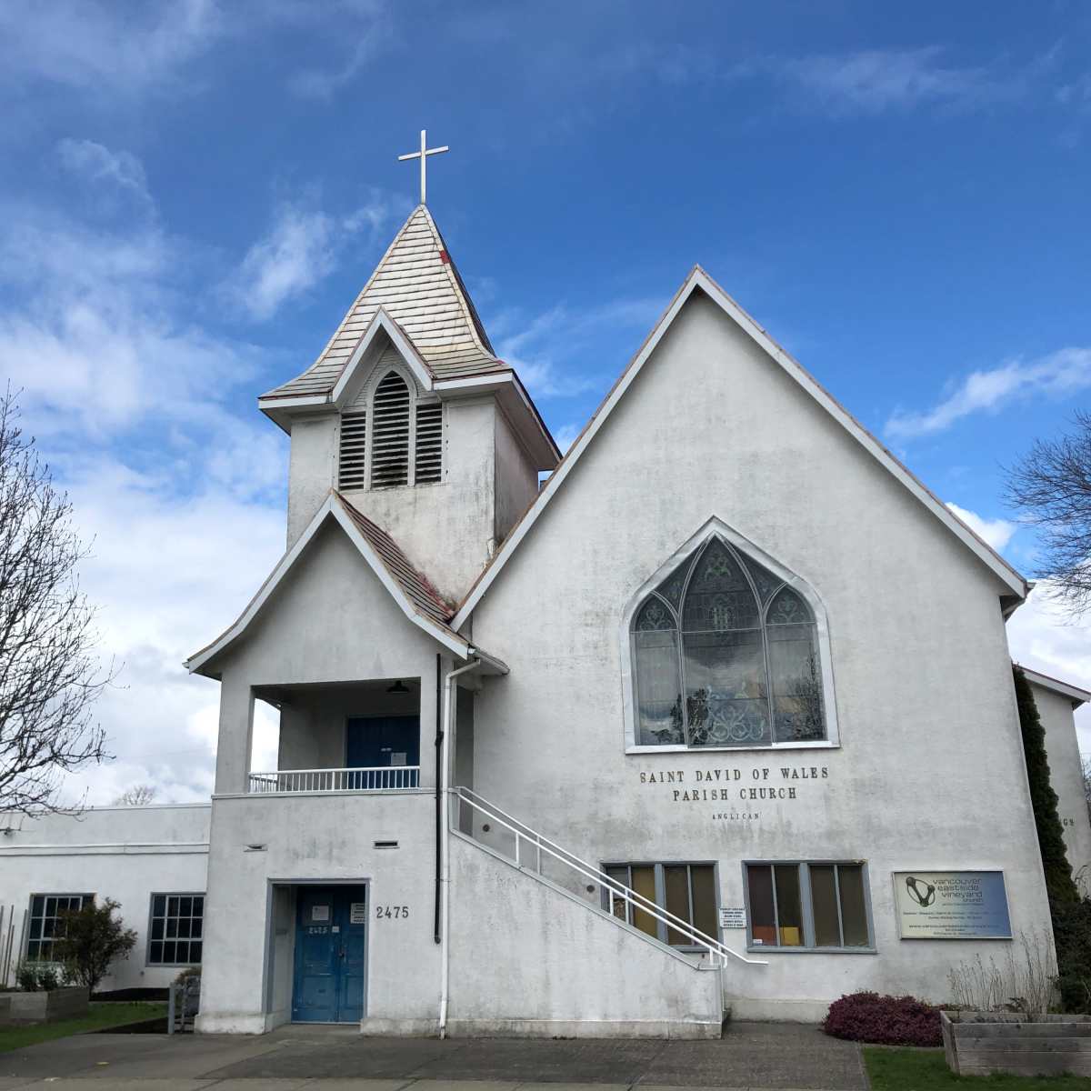 A white church building with a pointed roof, a cross on top, and a large stained glass window.
