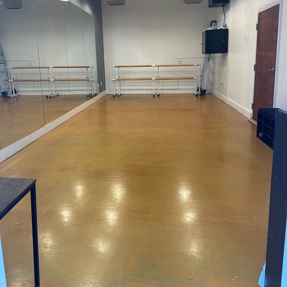 An empty dance studio with a wooden floor, mirrors on one wall, and overhead lighting.