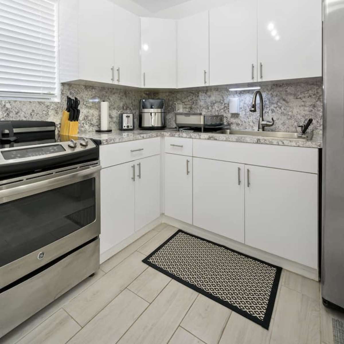 A modern kitchen features white cabinets, stainless steel appliances, and a gray granite countertop.