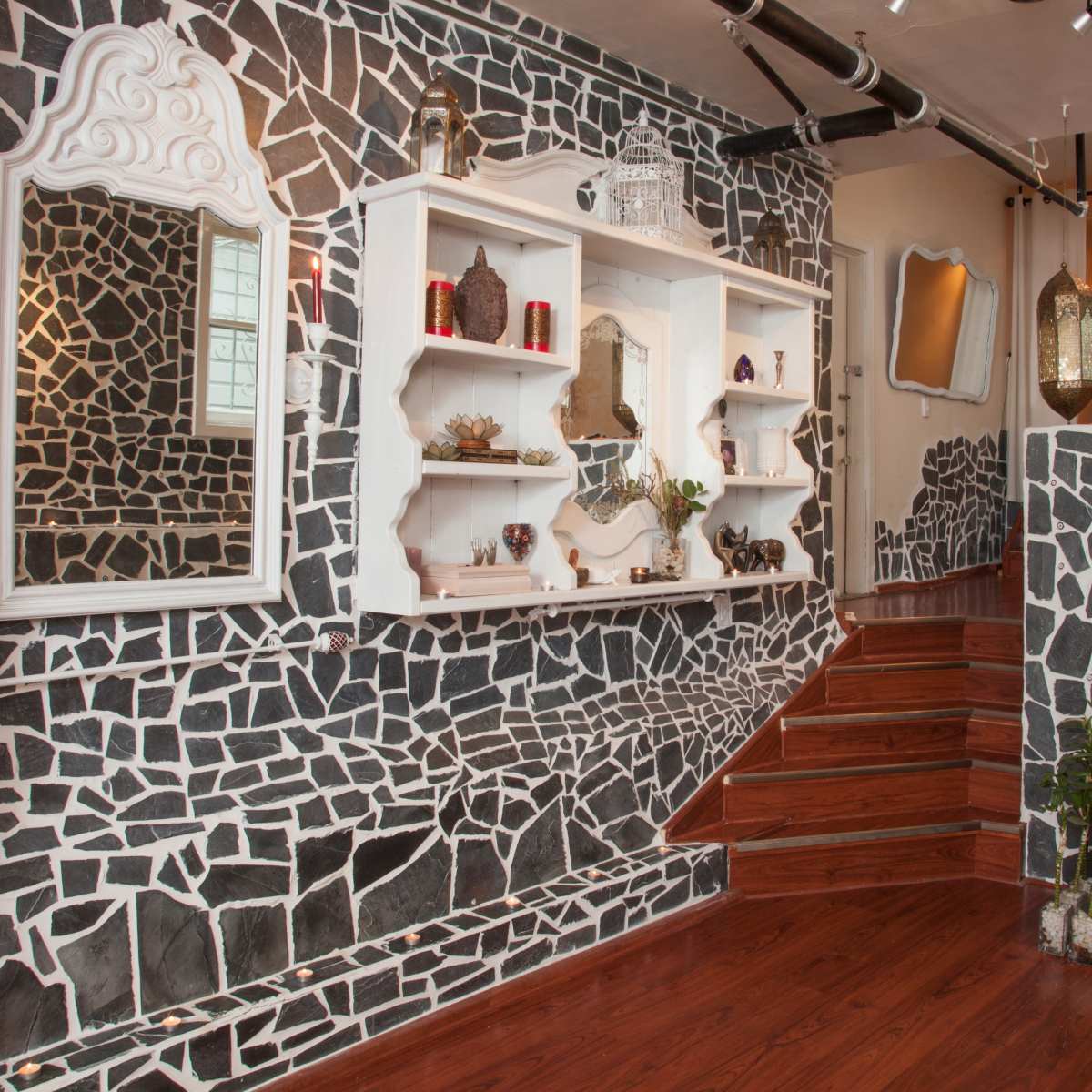 An interior space with a staircase, accentuated by a wall covered in black and white mosaic patterns and decorated shelves.
