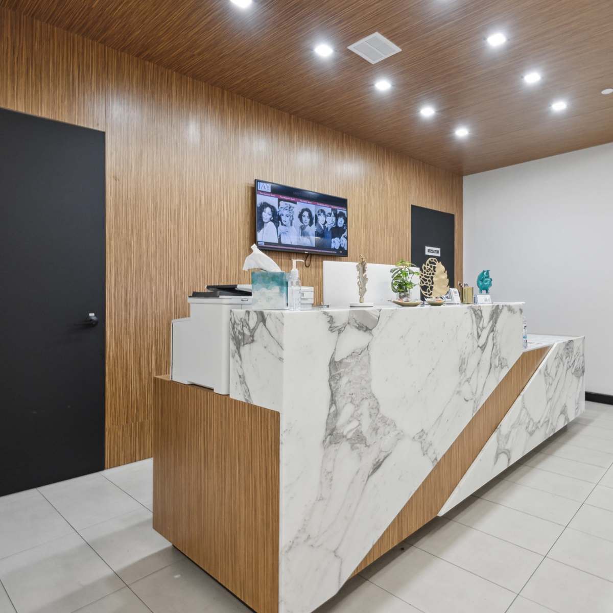 A modern reception area with a marble front desk, wooden paneling, and digital displays on the walls.