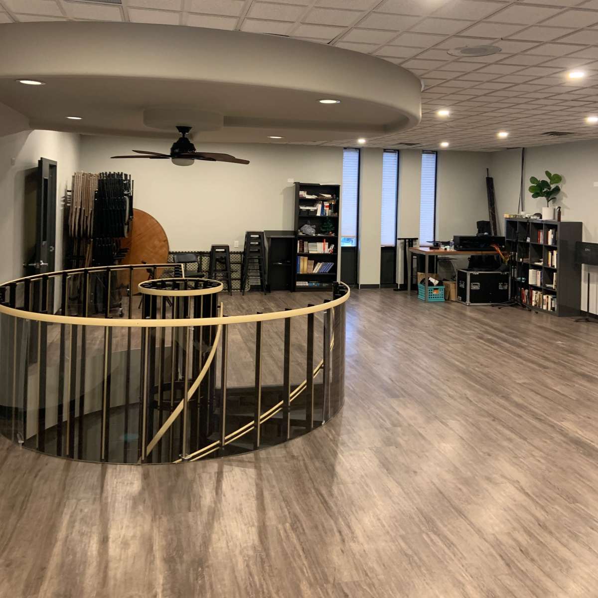 A spacious interior office with a circular balcony, wooden flooring, and rows of shelves filled with books.