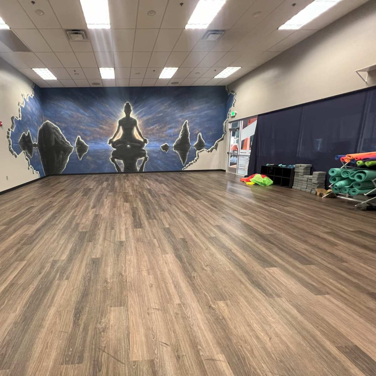 A spacious, empty yoga studio with a mural of a seated figure on a blue and black background.