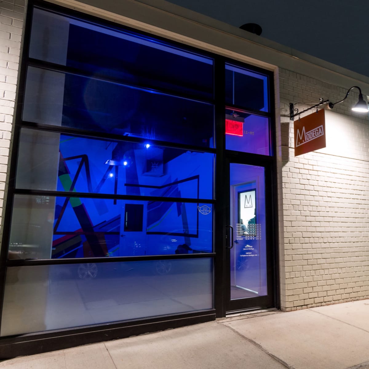 A modern storefront with large glass windows illuminated by blue light, featuring a sign that reads "M."