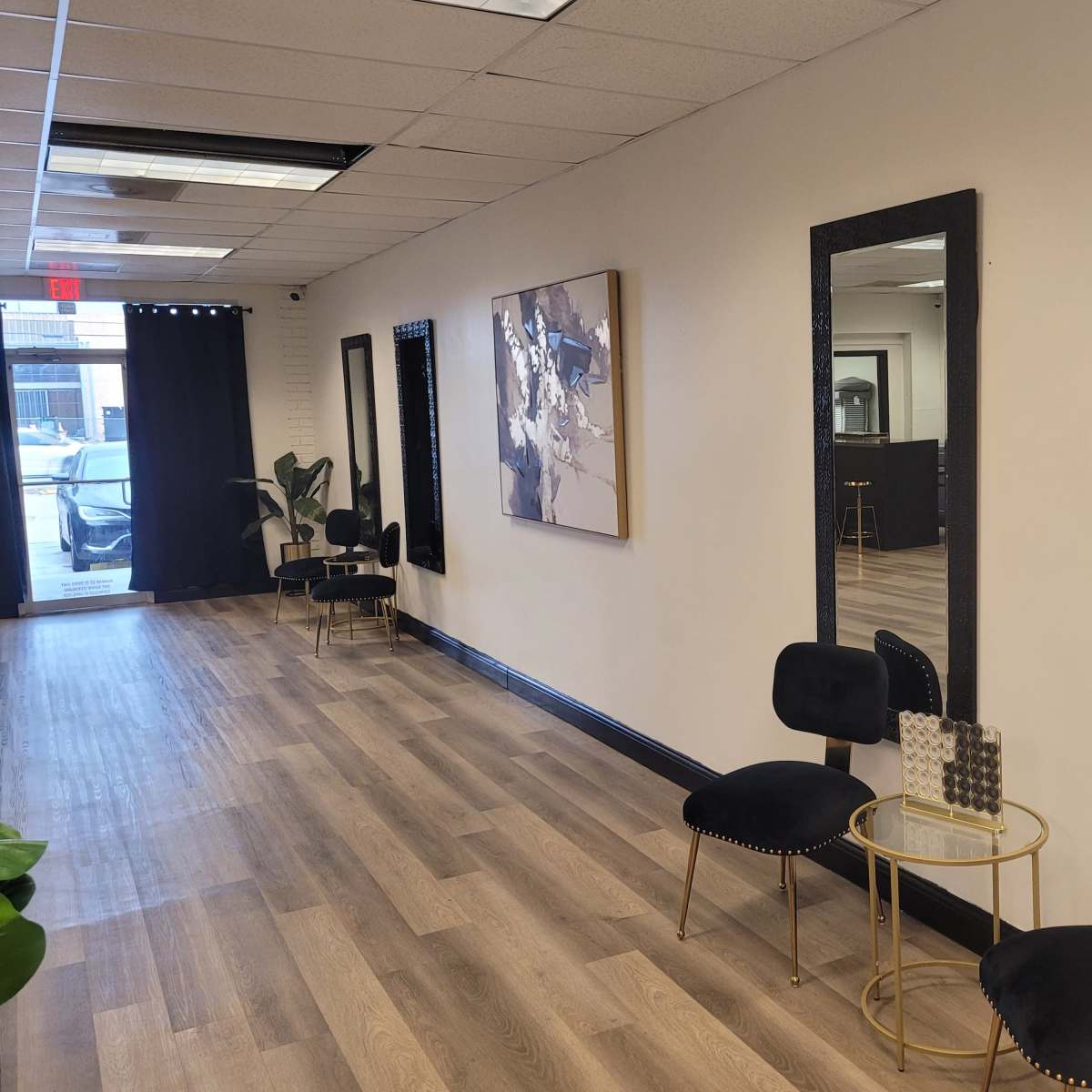 A well-lit hallway features two large mirrors, modern chairs, and a piece of abstract art on the wall.