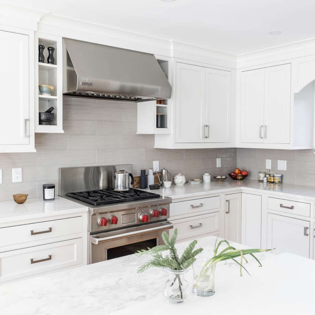 A modern kitchen features white cabinetry, a stainless steel refrigerator, and a gas stove beneath a metallic hood.