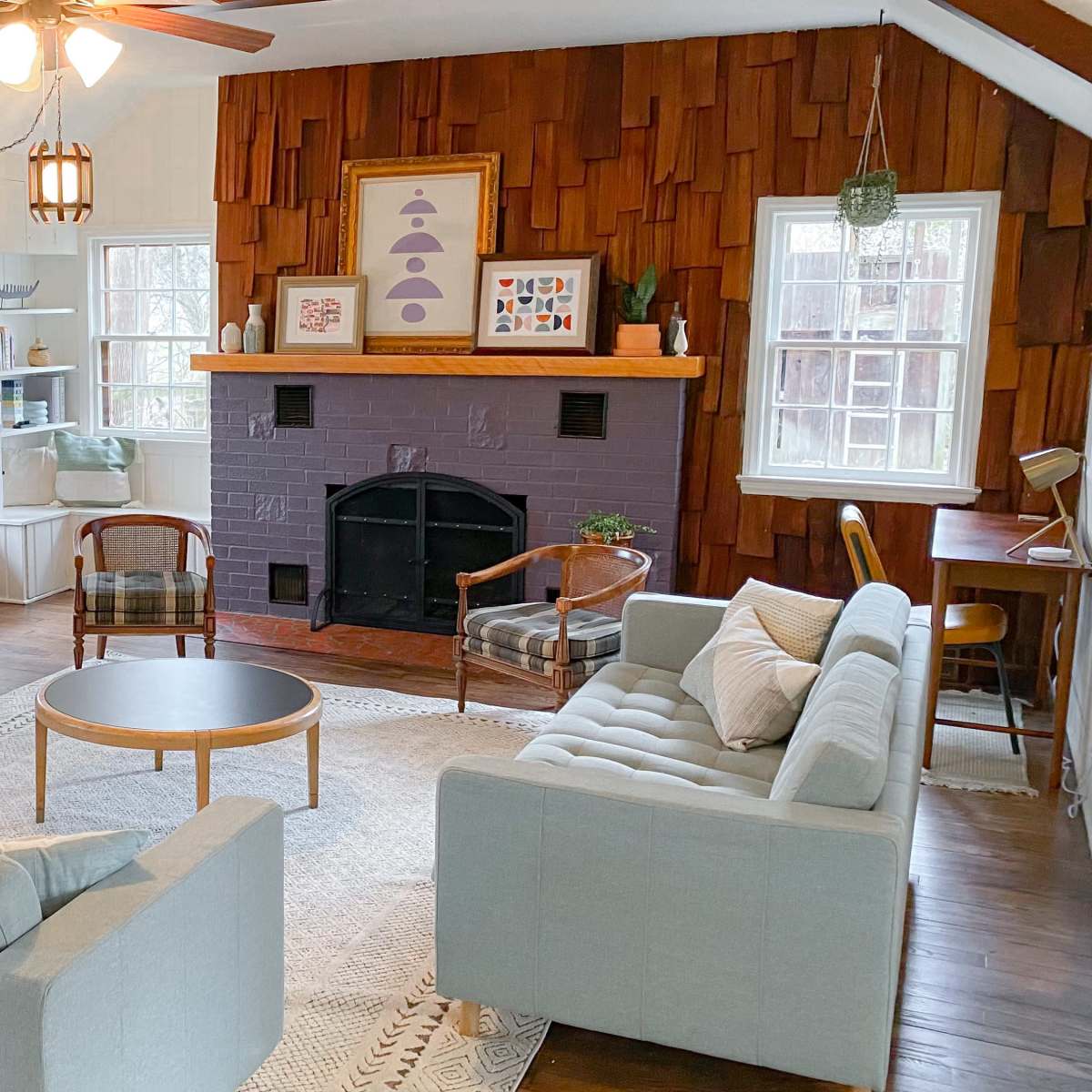 A cozy living room with two light blue sofas, a circular coffee table, a television on a stand, and a wooden accent wall featuring a fireplace.