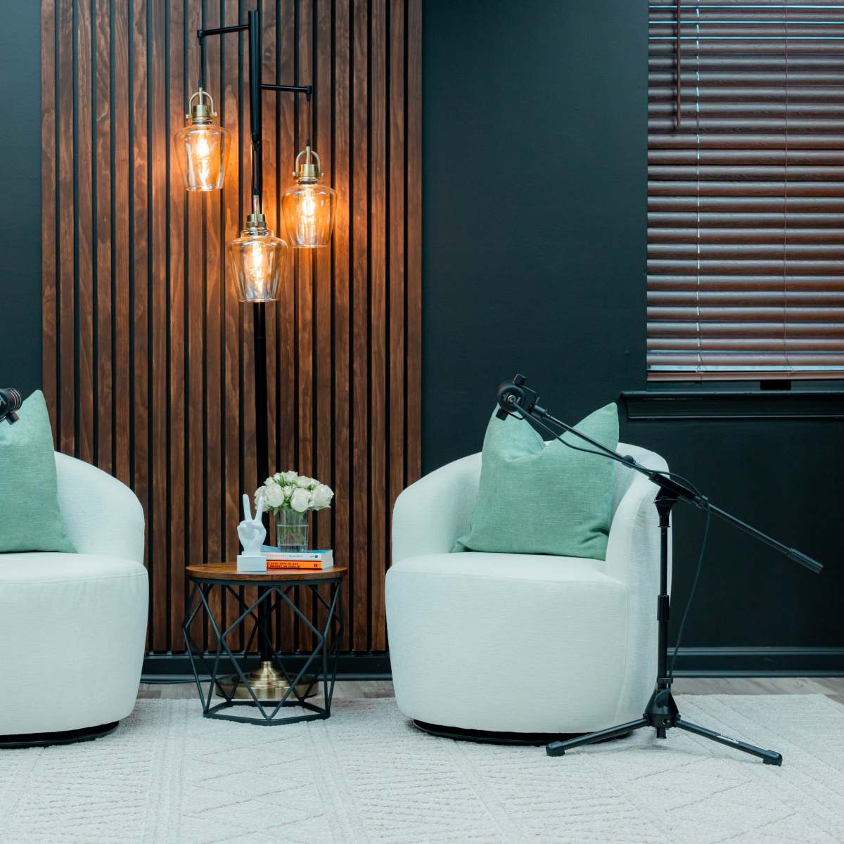 Two white chairs with green cushions positioned facing each other under a multi-light fixture, with a small table and floral arrangement between them.
