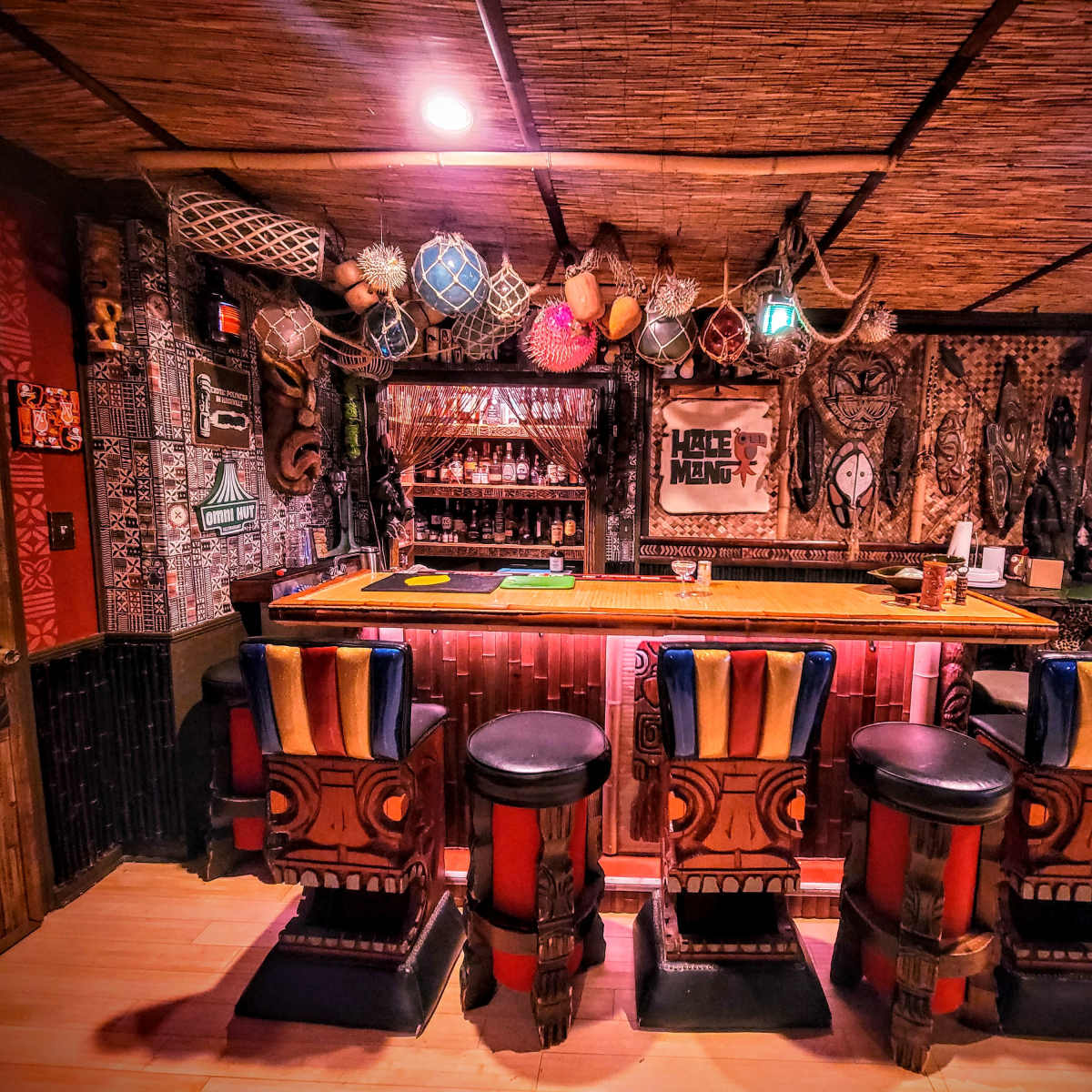 A tiki-style bar equipped with colorful stools and various decorative artifacts lining the walls and ceiling.