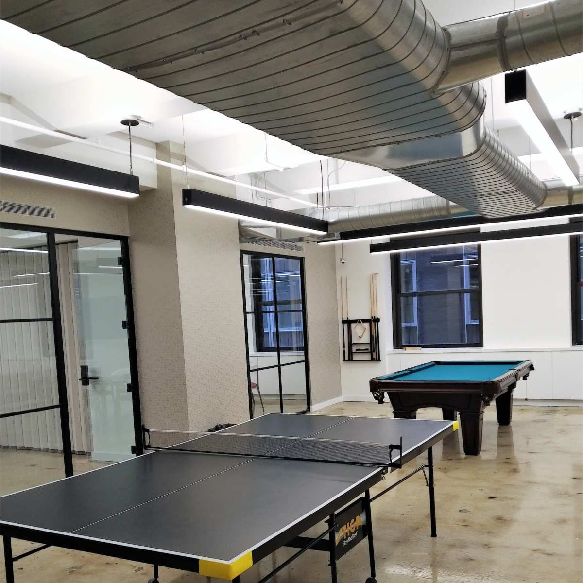 A recreational room with a ping pong table on the left and a pool table on the right, both situated on a polished concrete floor.