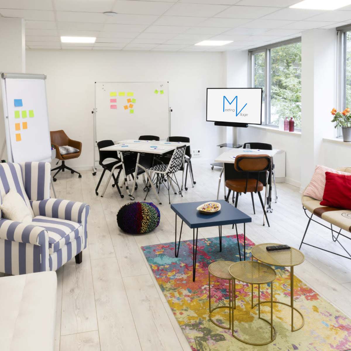 A modern office space with a seating area, a conference table, whiteboards, and large windows letting in natural light.