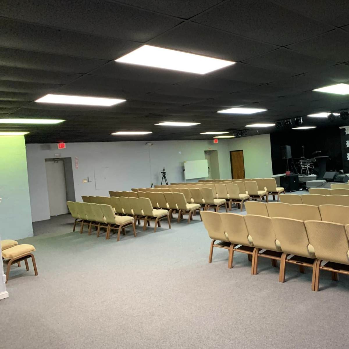 A spacious interior of a church or auditorium features rows of beige chairs facing a stage with audio equipment and lighting.