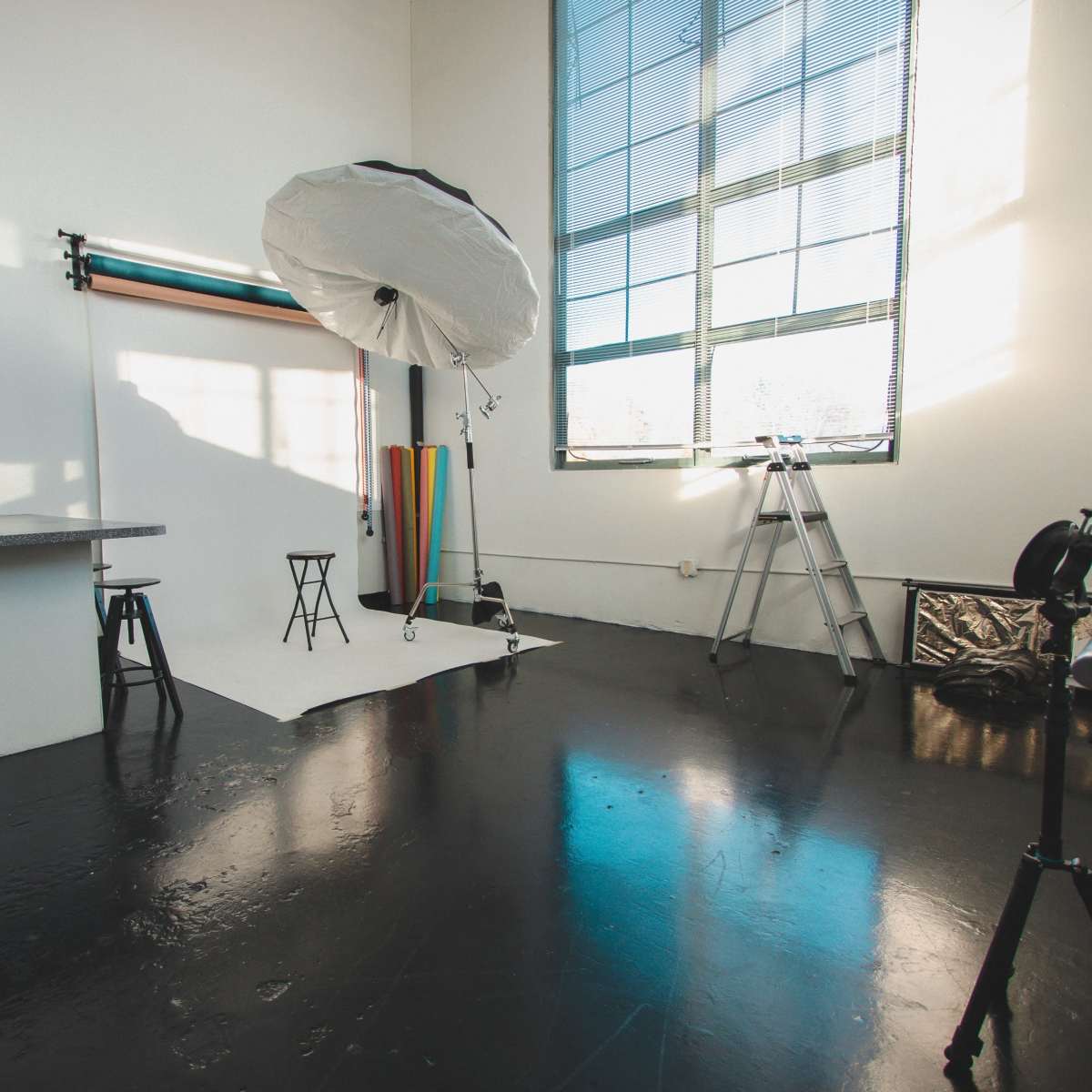 A well-lit photography studio featuring a backdrop, lighting equipment, and a ladder against the wall.
