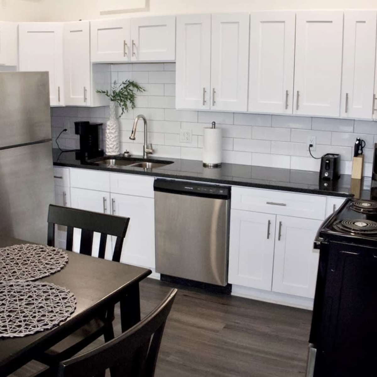 A modern kitchen featuring white cabinets, stainless steel appliances, a black countertop, and a dining table with circular placemats.