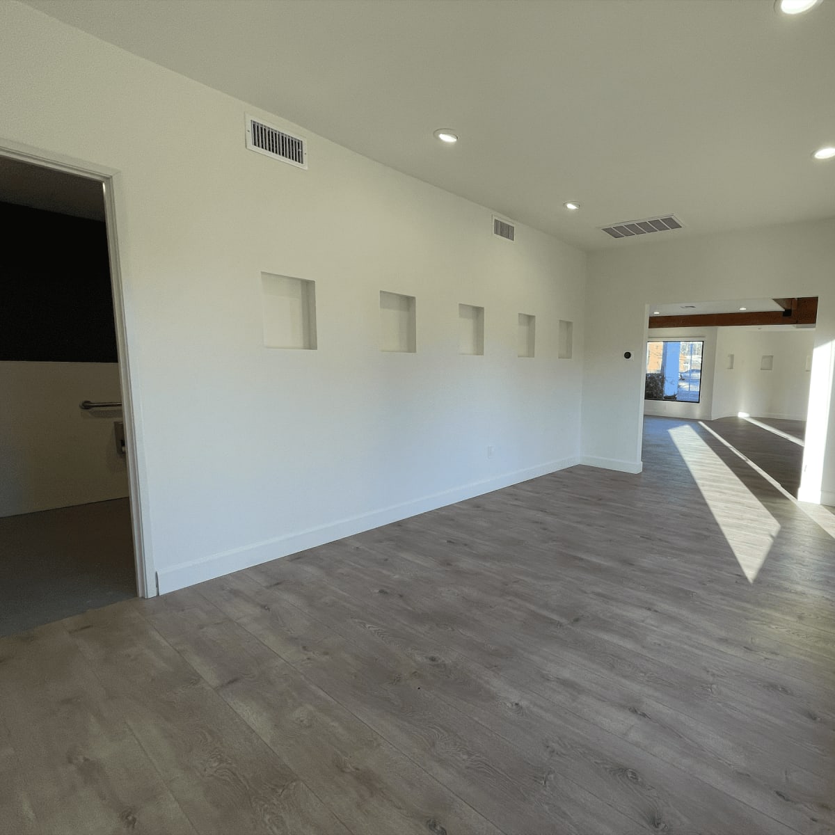 A bright, empty room with light-colored walls, a wooden floor, and several square recessed niches on one wall.
