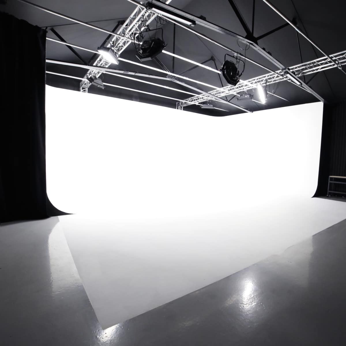 A photography studio with a large white backdrop and polished concrete floor under bright overhead lighting.