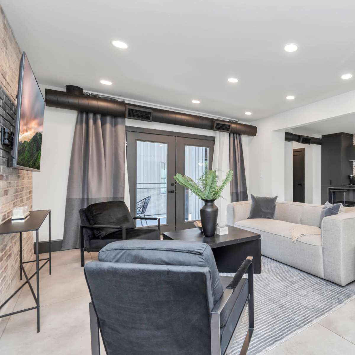 A modern living area featuring a sectional sofa, two chairs, a coffee table, and a kitchen with a brick backsplash and stainless steel appliances.