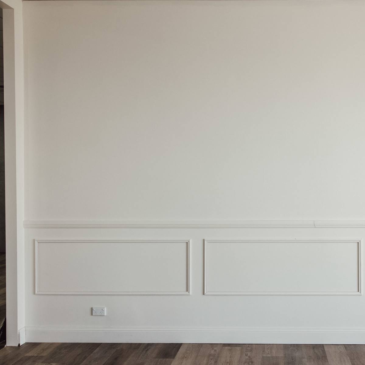 A plain white wall with decorative molding and wooden flooring.
