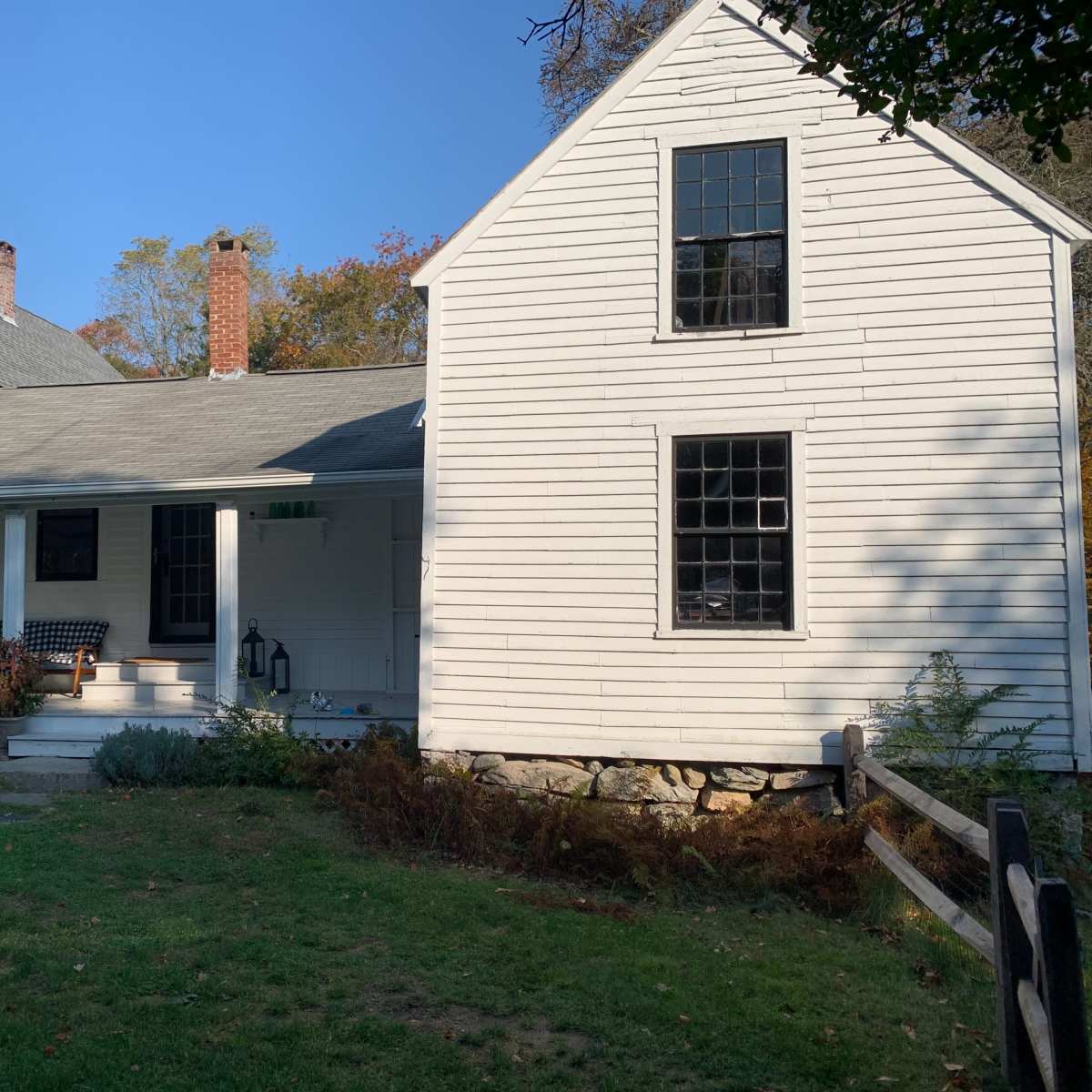 A white, two-story house with a porch and a sloped roof, surrounded by grass and trees.