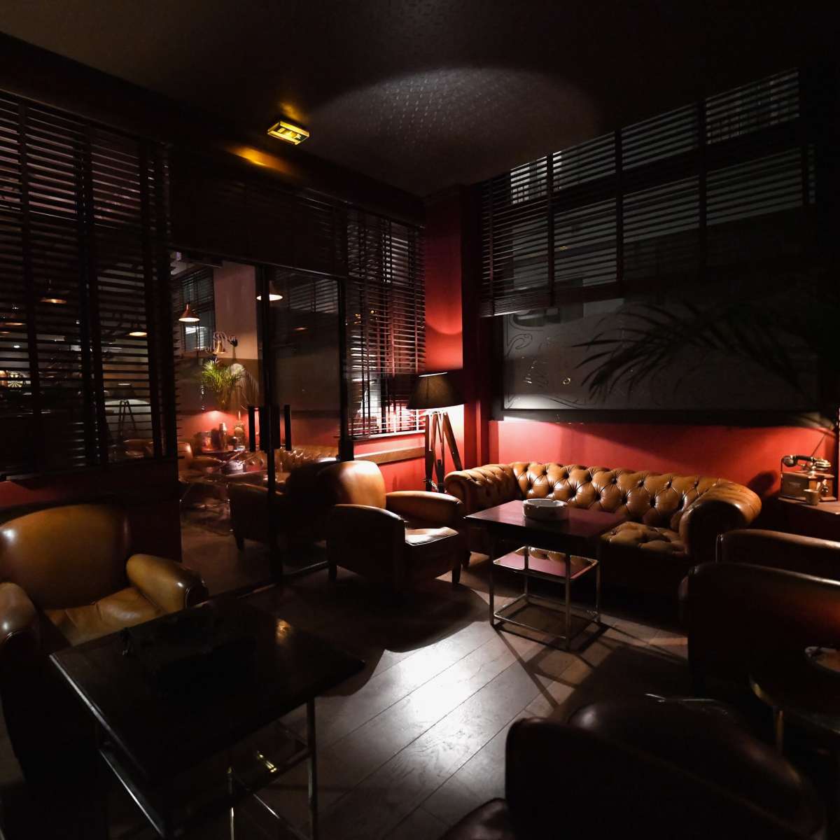 A cozy lounge area with leather sofas, low lighting, and large windows partially covered by wooden blinds.