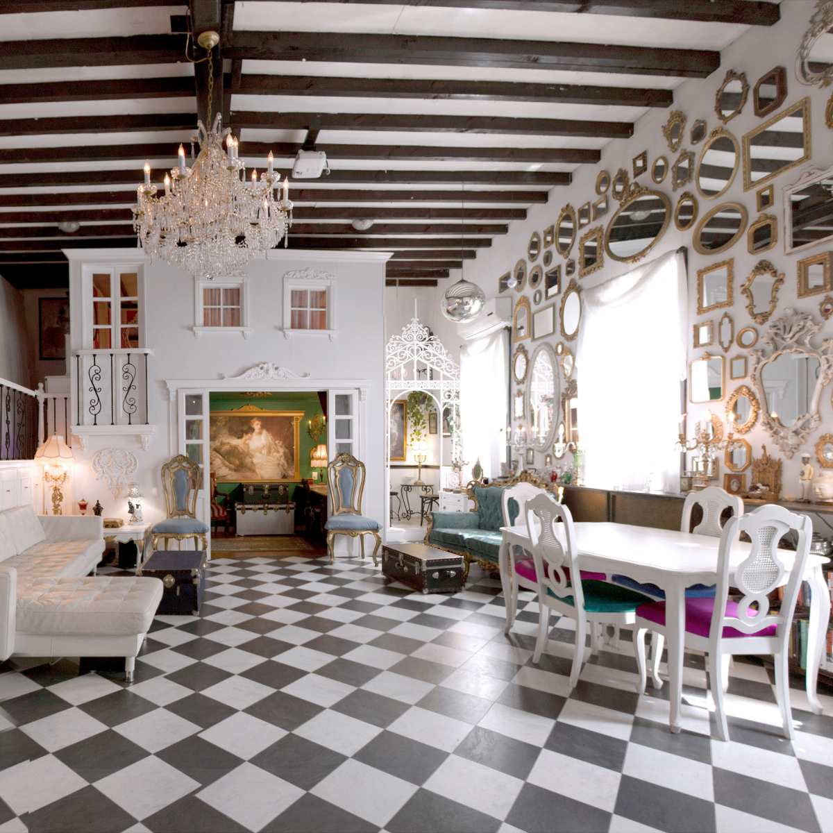 A spacious, elegantly decorated room featuring checkered flooring, a white sofa, a chandelier, and numerous mirrors on the walls.