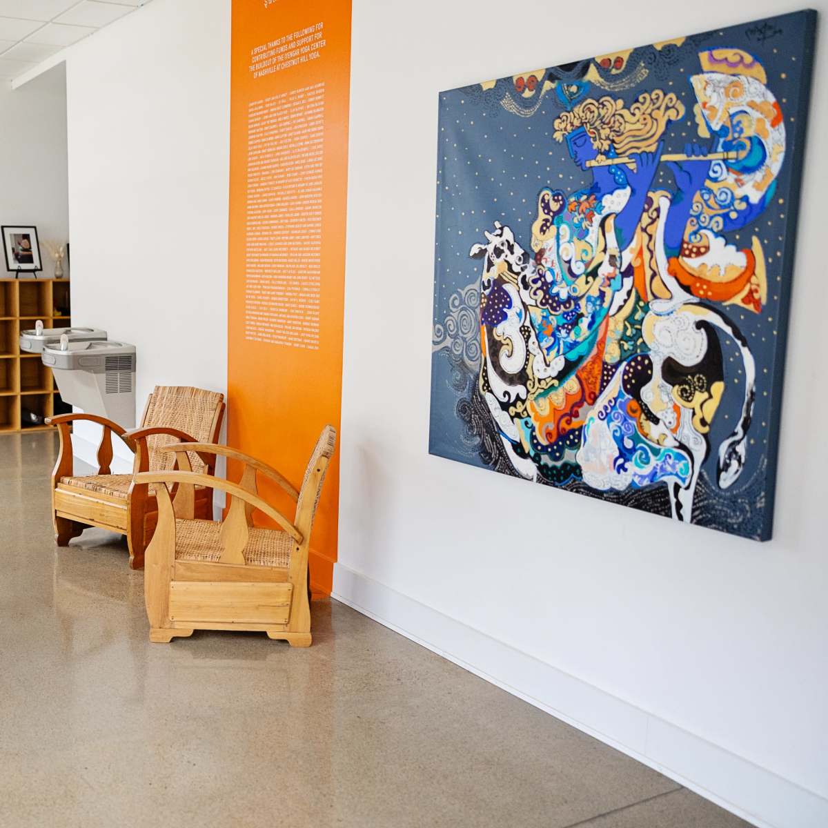 A hallway features wooden chairs, a vibrant artwork on the wall, and bookshelves filled with books.