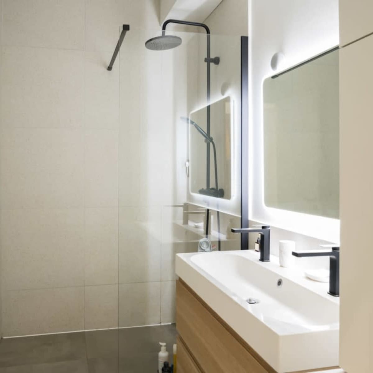 A modern bathroom with a glass shower, a backlit mirror, and a wooden vanity with black fixtures.