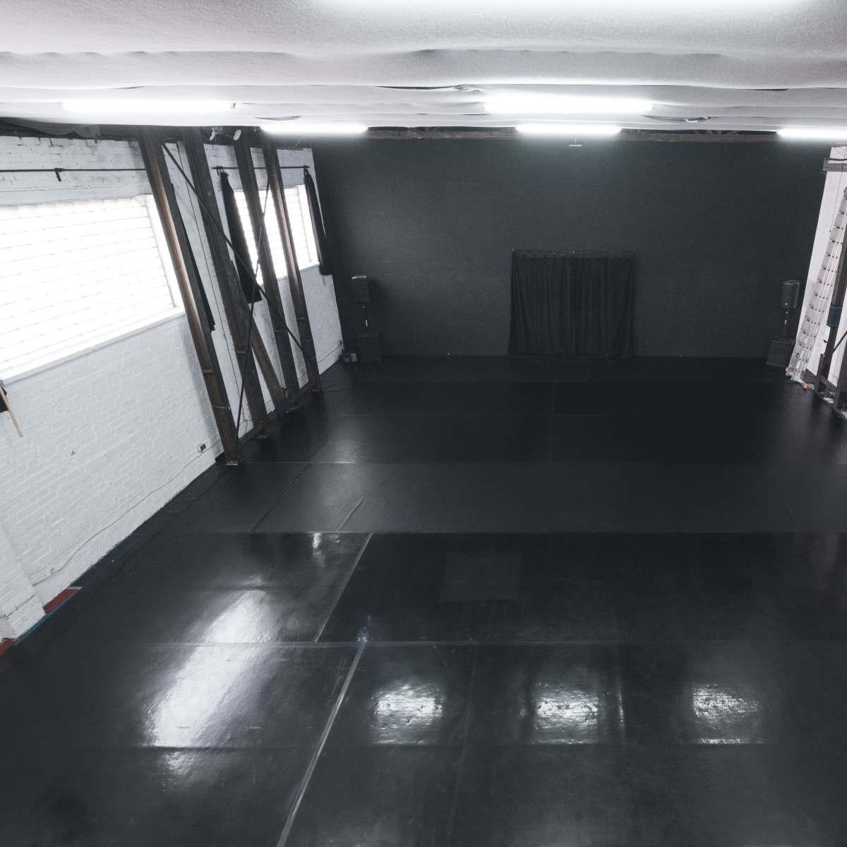 A spacious, empty room with a polished black floor and industrial-style walls.