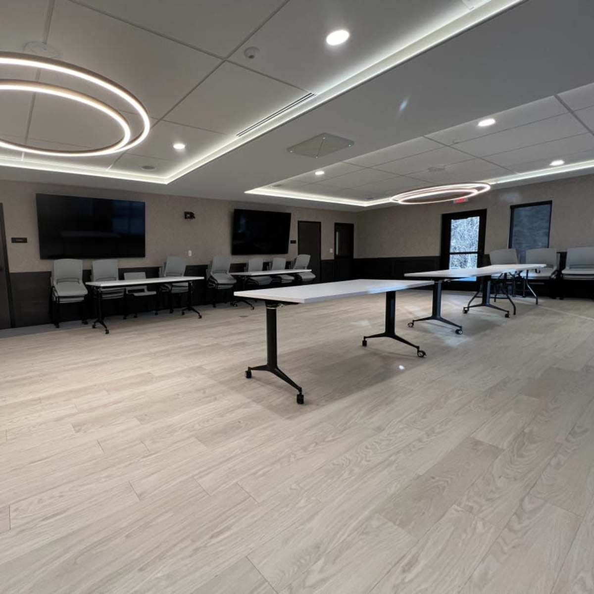 A modern conference room featuring light wood flooring, sleek tables, and circular ceiling lights.