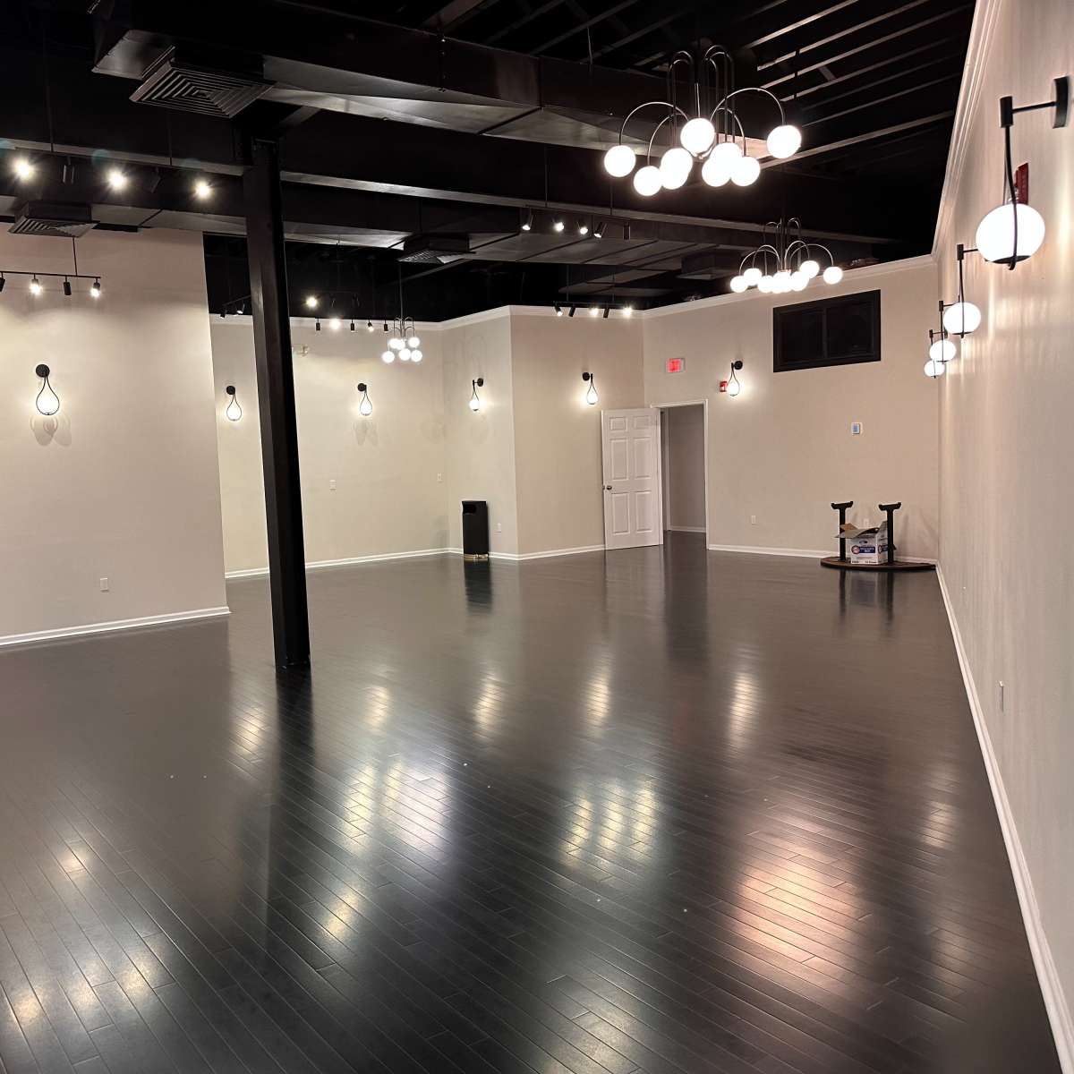A spacious, empty interior room with dark hardwood floors and several light fixtures hanging from the ceiling.