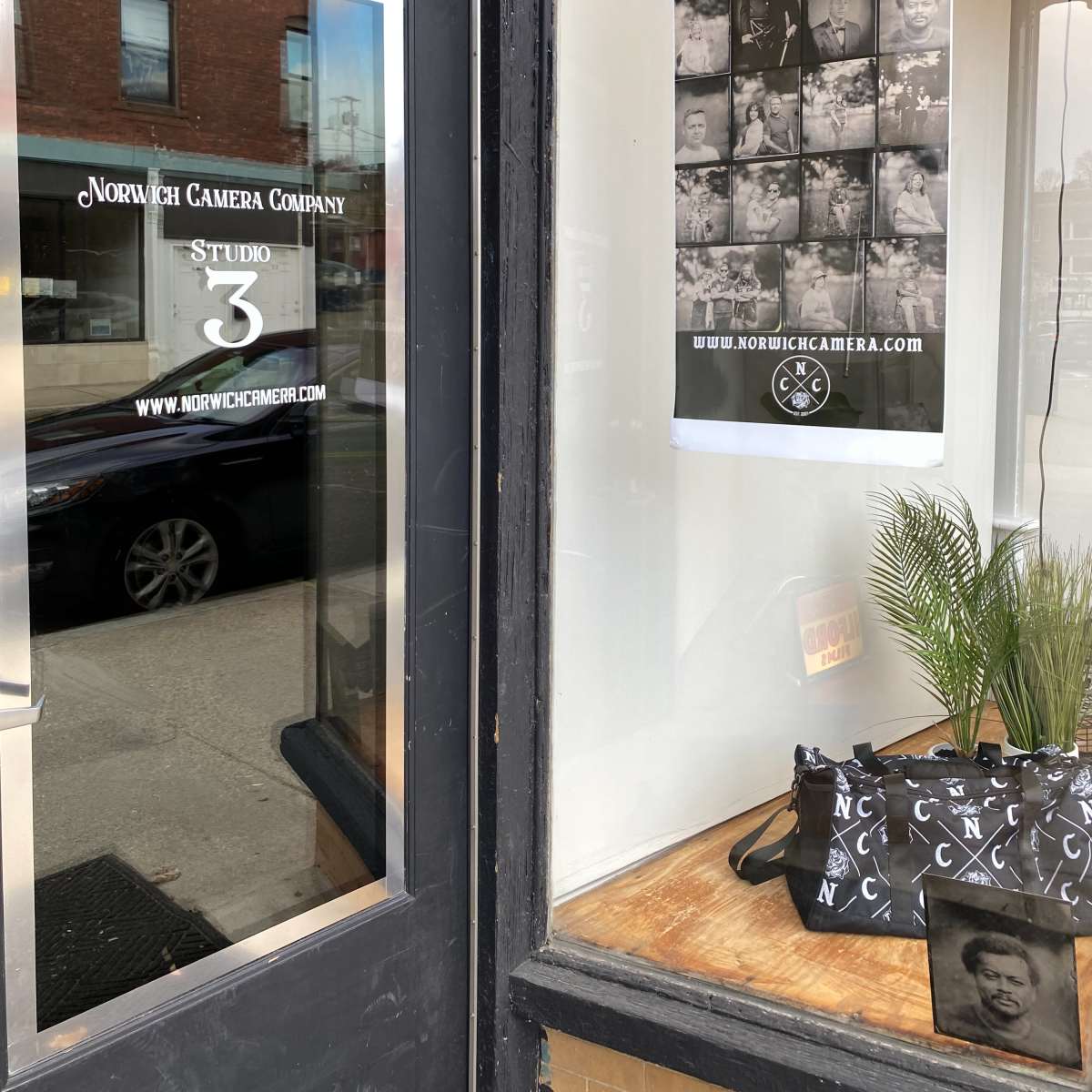 The exterior of the Norwich Camera Company, featuring a window display with a poster and a decorative plant.
