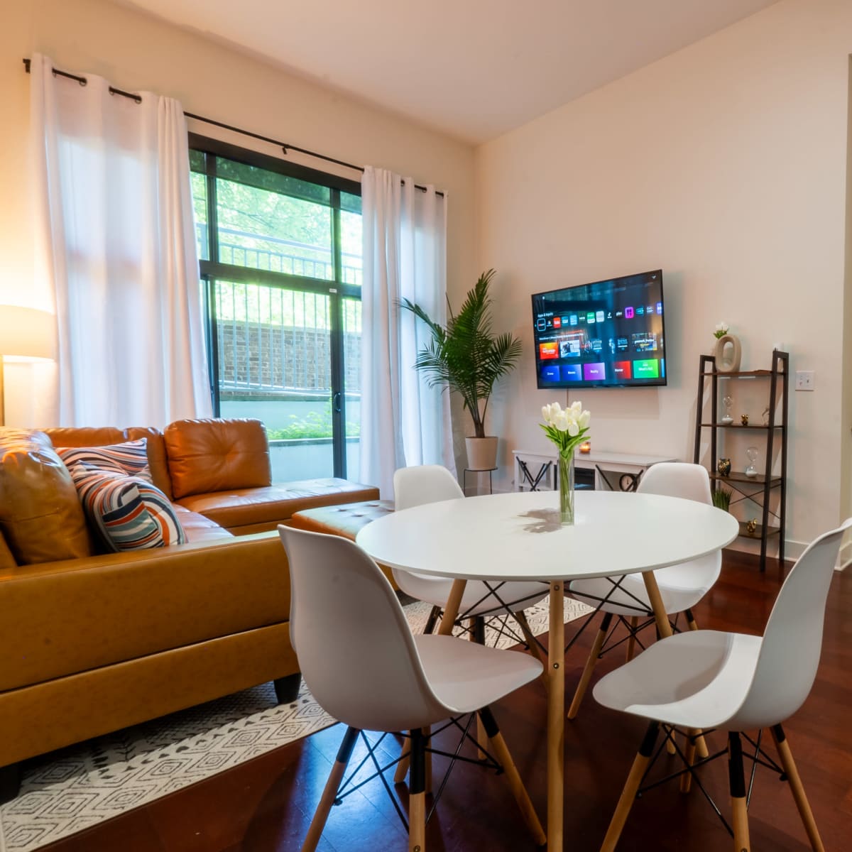 A modern living space featuring a yellow sofa, a round dining table with white chairs, and a wall-mounted television.