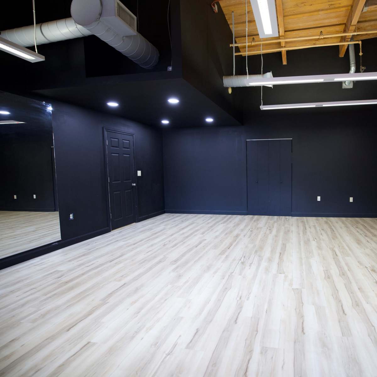 An empty room with hardwood flooring, exposed brick walls, and a large mirror on one side.