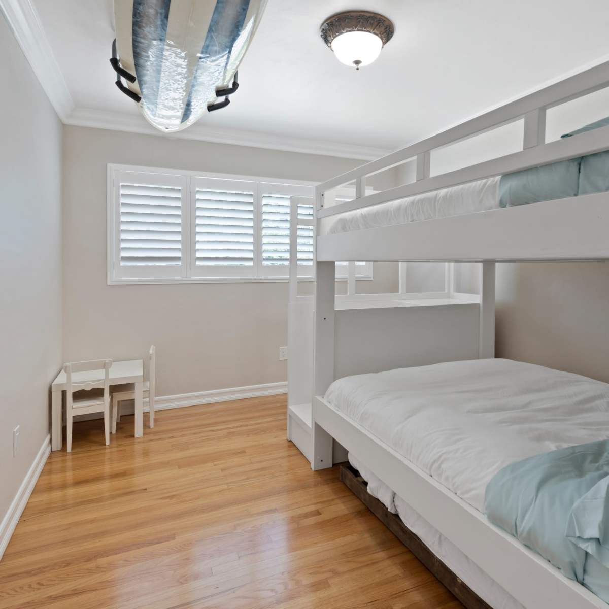 A well-lit bedroom featuring a bunk bed with light blue bedding and a small table and chairs against one wall.