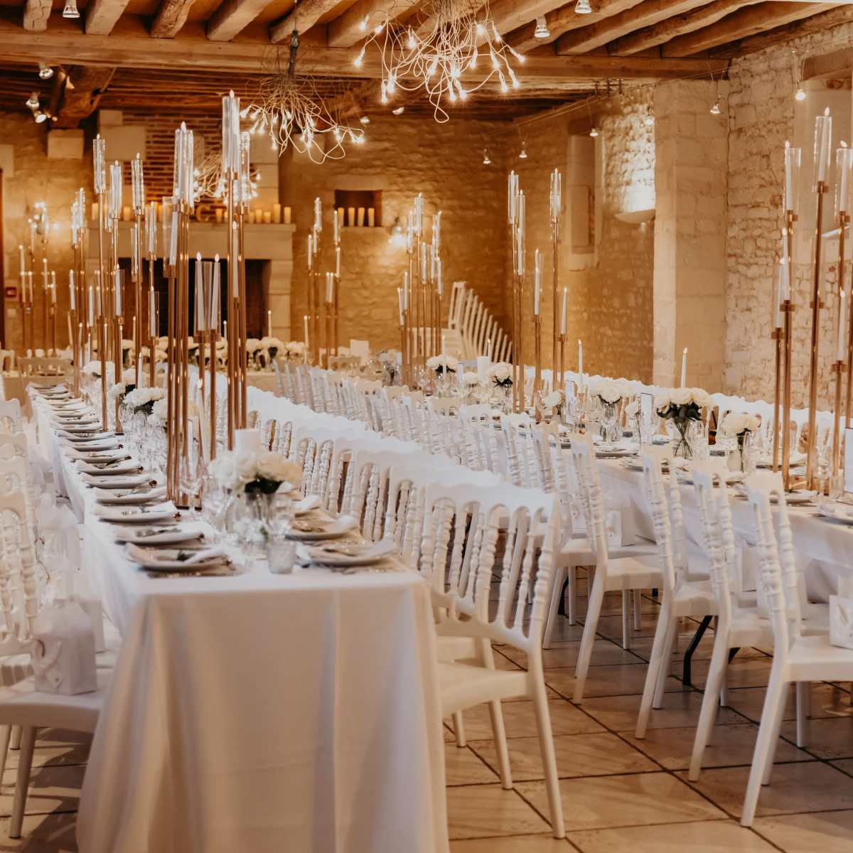 A dining hall set for a formal event, featuring long tables covered in white tablecloths and adorned with tall candle holders.