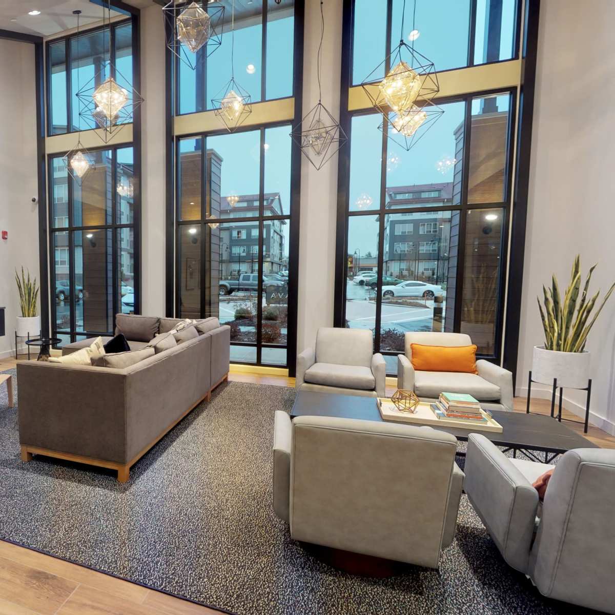 A modern lounge area featuring large windows, a television mounted on a wall, stylish light fixtures, and a mix of seating arrangements with a coffee table.