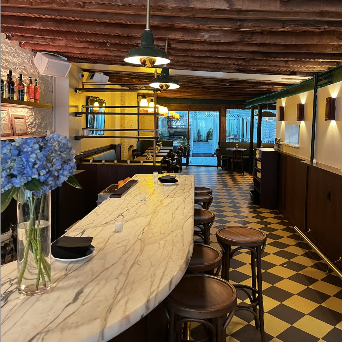 The interior of a restaurant with a marble bar, wooden stools, and a checkered floor.