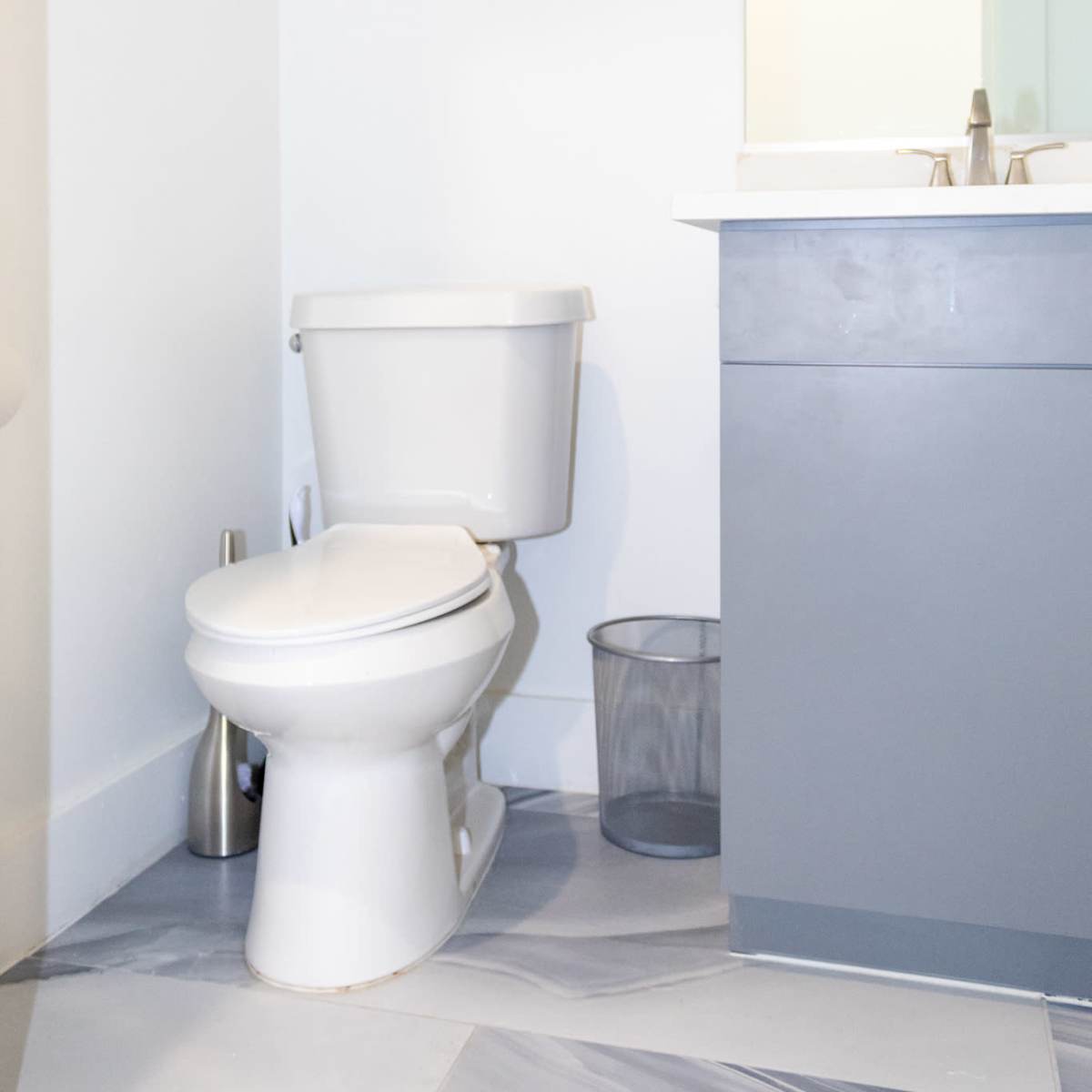 A bathroom featuring a white toilet, a gray vanity with a sink, and three decorative mirrors mounted on the wall.