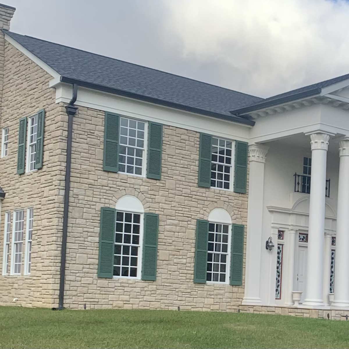 A large, two-story house featuring a stone exterior, white columns, and green shutters.
